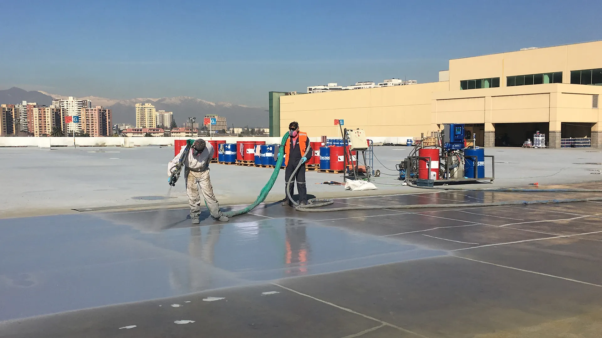 Operarios profesionales aplicando recubrimiento de poliurea industrial en una superficie de gran extensión con equipo especializado, destacando la precisión técnica y el uso de elementos de protección personal en una obra de ingeniería a cielo abierto.